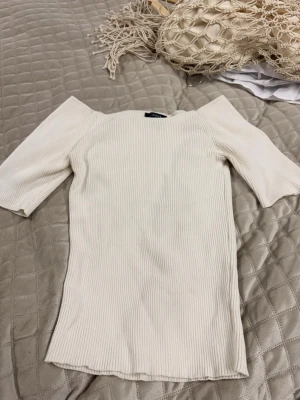 Ribbad offshoulder topp i beige - Superfin ribbad topp från Lindex i beige med offshoulder-modell och halvlånga ärmar. Perfekt för dig som gillar en stilren och enkel look. Materialet är mjukt och stretchigt för en bekväm passform.