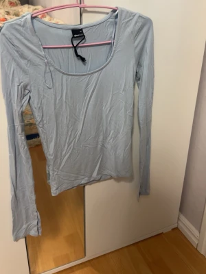 Ljusblå långärmad topp  - En enkel och stilren ljusblå långärmad topp från gina . Toppen har en rund, djup urringning och är tillverkad i ett mjukt och stretchigt material som sitter skönt mot kroppen. Perfekt att matcha med jeans eller kjol.