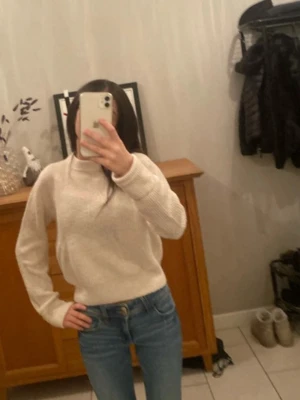 Beige stickad tröja med rund hals - Mysig beige stickad tröja med rund hals och långa ärmar. Tröjan har en enkel, klassisk design och är perfekt att matcha med jeans för en avslappnad look. Materialet ser ut att vara mjukt och bekvämt.