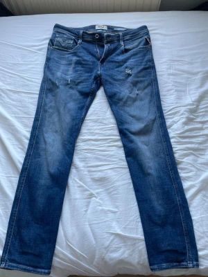 Blå Replay Anbass jeans med slitningar - Snygga blå jeans från Replay I modellen anbass med diskreta slitningar framtill. Perfekta för en avslappnad och trendig look. Storlek W32 L32, pris går att diskuteras!