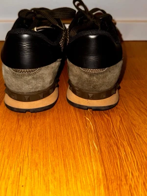 Valentino Rockrunners - Säljer ett par snygga Valentino sneakers med camomönster i grönt, svart och beige. Skorna har detaljer i mocka, mesh och läder samt nitar på sulan. Perfekta för dig som vill ha en trendig sko. Bra skick men har en lös söm som visas i bild 6. OG Box och dustbags följer med.