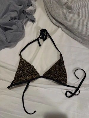 Leopardmönstrad bikini med svarta band och en svart underdel - Snygg bikini med trekantsöverdel i leopardmönster och svarta knytband. Underdelen är enkel och svart med hög skärning. Perfekt för stranden eller poolen och ger en trendig look. Sen kommer de en svart underdel med. Överdelen är S och underdelen är M