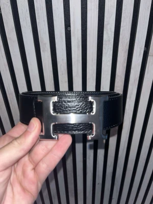 Svart kärp med H-spänne - Säljer ett svart skärp med det ikoniska H-spännet i silverfärgad metall. Bältet har en stilren, lyxig vibe som lyfter vilken outfit som helst.