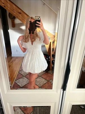 Vit kort klänning med broderi - Superfin vit kortklänning med v-ringning och puffärmar. Klänningen har broderade detaljer och en lätt utsvängd kjol som ger en söt och somrig look. Perfekt till ex studenten!!