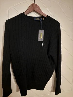 Svart stickad tröja Polo Ralph Lauren - Snygg svart stickad tröja från Polo Ralph Lauren med klassisk kabelstickning och rund hals.                Storlek L men sitter som Medium i storlek              Säljer pågrund av att storleken var för liten på mig (knappt använd tröja)