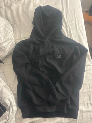 Hov1 hoodie - Svart hoodie från Hov1 med liten krona broderad på bröstet och stort turnétryck på ryggen med texten 'Vi Dansar Vidare I Livet' och turnédatum. Klassisk passform med huva och ribbade muddar. Perfekt för dig som gillar svensk musik och streetwear.