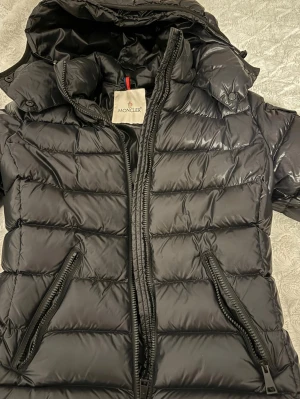 Moncler bady - Moncler Bady i svart, bra skick. QR/Certilogo finns och kan verifieras. Fått i present, därför saknas kvitto. Enda anmärkningen är att draget på ena fickans dragkedja saknas, men funktionen är kvar. Kan skickas fler bilder vid större intresse/verifering.  Nypris ca 10 000 kr. 