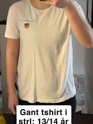 Vit Gant t-shirt med logga - Vit t-shirt från Gant med klassisk rund hals och liten broderad logga med sköld på bröstet. Tillverkad i mjuk bomull och har en enkel, stilren design som passar till det mesta. 