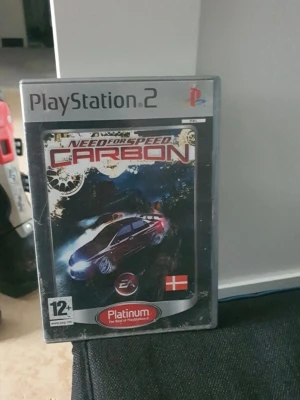 Need for Speed Carbon PS2 - Need for Speed Carbon till PlayStation 2 är ett racingspel där du tävlar med snabba bilar genom stadens gator. Omslaget är svart med en röd sportbil och spelet är en Platinum-utgåva. Perfekt för dig som gillar fartfyllda bilspel och street racing.