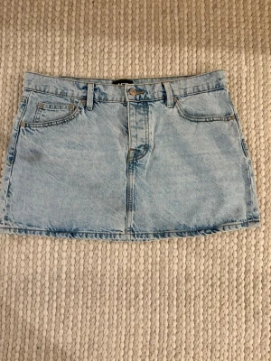 Ljusblå jeanskjol från 157 - Säljer en klassisk ljusblå jeanskjol från 157, modell Maddy. Kjolen har fem fickor, bälteshällor och stängs med knapp och dragkedja framtill. Perfekt basplagg till garderoben och enkel att styla med olika toppar. 