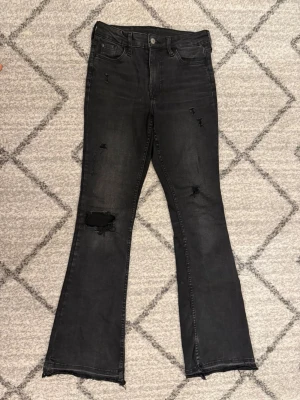 Svarta utsvängda jeans med slitningar - Snygga svarta jeans med utsvängda ben och flera coola slitningar, jeansen är midwaits men går att vika ner till lowaist. Jeansen är uppsprättade längst ner. Tryck inte på Köp innan ni kontaktat mig!