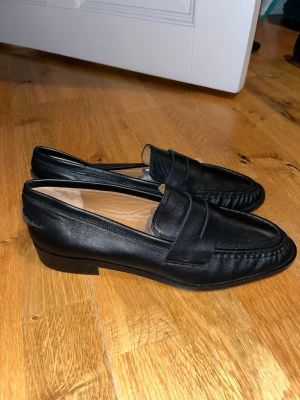 Svarta airola nappa loafers från ATP Atelier - Stilrena svarta loafers från ATP Atelier i slätt läder. Klassisk penny loafer-design med rundad tå och diskret söm längs kanten. Nypris 4899kr Skorna har låg klack och en elegant, tidlös look som passar till många olika outfits. Har ej original låda tyvärr. Skriv om du har några frågor eller vill ha bilder💕