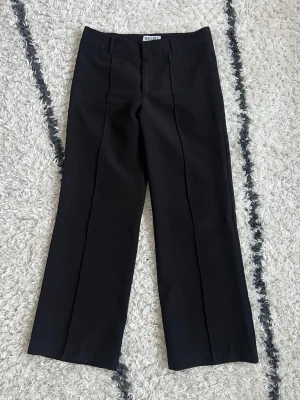 Svarta kostymbyxor från Madlady - Snygga svarta lågmidjade kostymbyxor  från Madlady med pressveck framtill och raka ben. Modell ”Hazel”. Byxorna har hällor för skärp och klassisk midja. Lite noppriga. Storlek 34 / Ex-short.
