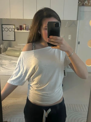 Vit off-shoulder t-shirt - Använd få gånger, men ser jättebra ut. Säljer en vit t-shirt med off-shoulder  design och lös passform. T-shirten har korta ärmar och är tillverkad i ett mjukt, tunt material som känns skönt mot huden. Perfekt för en avslappnad och trendig look. 🥰🥰