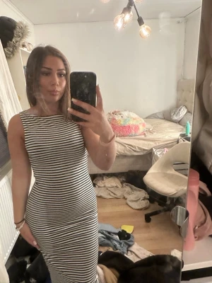 Randig långklänning i bomull - Snygg långklänning med svarta och vita ränder. Klänningen är ärmlös och har en tight passform som framhäver figuren. Perfekt för dig som gillar en enkel men stilren look.