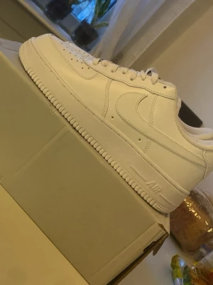 Nike Air Force 1 vita sneakers - Klassiska helvita Nike Air Force 1 sneakers i lågt utförande. Skorna har en stilren design med perforerad tå, vita skosnören och Nike Swoosh på sidan. Tillverkade i läder med en robust sula och metallbricka på snörningen. Perfekta för en clean och tidlös look. Helt o använda!