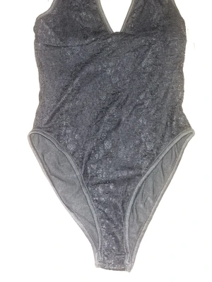 Svart body med djup ringning - Snygg svart body med djup V-ringning med spets struktur i tyget. Klassisk modell med hög benskärning och smala axelband. Perfekt för sommardagar. Materialet känns mjukt och stretchigt för en bekväm passform. Aldrig andvänd!