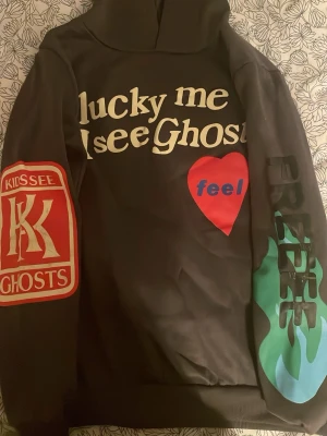 Kanye west Lucky Me I See Ghosts hoodie - Säljer en svart hoodie från Kids See Ghosts med tryck fram och bak. Framsidan har texten 'lucky me I see Ghosts', ett rött hjärta med 'feel', samt färgglada detaljer på ärmarna. Baksidan har 'camp flog Gnaw nov 11' i stor text. Perfekt för dig som gillar streetwear och unika prints. Se defekterna på bilderna+tyget är tunt därav det billiga priset som självklart kan diskuteras. Har ni några frågor eller funderingar är det bara att ni hör av er💝🤗