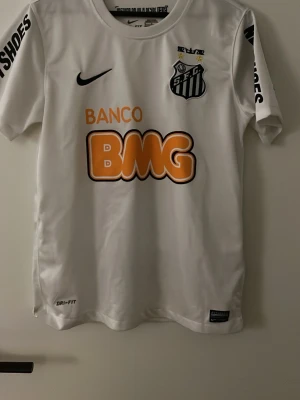 Vit Santos FC Neymar Jr matchtröja - Säljer en vit Santos FC matchtröja från Nike med Neymar Jr och nummer 11 på ryggen. Tröjan har tryckta sponsorer, klubbmärke på bröstet och Dri-FIT-material som andas. Perfekt för dig som älskar brasiliansk fotboll och vill ha en ikonisk supportertröja. Trycket på baksidan är lite buckligt men annars inga större skador