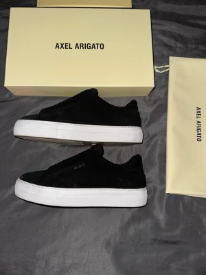 Svarta sneakers från Axel Arigato - Stilrena svarta sneakers från Axel Arigato i mocka med vit tjock sula. Klassisk låg modell med minimalistisk design och diskret logga på sidan. Perfekta för dig som gillar en clean och modern look. Storlek 41