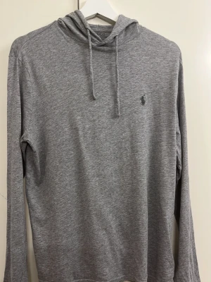Grå hoodie från Polo Ralph Lauren - Snygg grå hoodie från Polo Ralph Lauren med klassisk huva. Tillverkad i mjukt och tunt material, perfekt för en avslappnad stil. Liten broderad logga på bröstet ger en clean och stilren look. Långärmad och enkel att matcha till det mesta. Skriv vid minsta fundering😊
