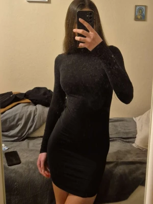 Svart tight långärmad klänning - Säljer en svart, figurnära klänning med lång ärm och rund hals. Klänningen är kort och har en enkel, stilren design som passar perfekt till olika tillfällen. Materialet känns stretchigt och bekvämt. Passar även S! 