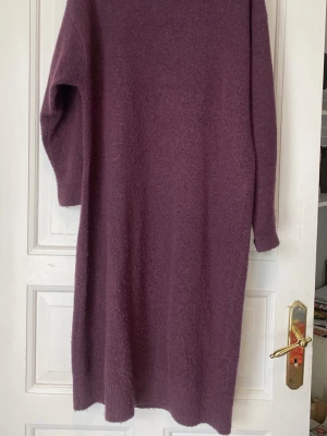 Lila stickad klänning från Monki - Mysig lila stickad klänning från Monki med rund halsringning och långa ärmar. Klänningen har en rak passform och är gjord i ett mjukt, fluffigt material som känns skönt mot huden. Perfekt för lager på lager och en chill look.