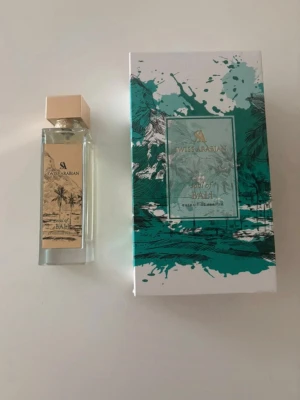 Swiss Arabian Bali Eau de Parfum - Upptäck Swiss Arabian Bali Eau de Parfum med en elegant rektangulär glasflaska och beige lock. Förpackningen har tropiskt inspirerad design i grönt och vitt. Perfekt för dig som vill ha en unik och fräsch doftupplevelse. + Aqua dubai 100ml