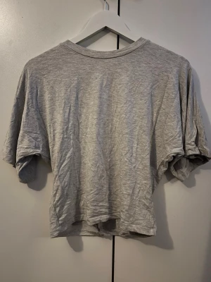 Ljusgrå basic t-shirt i bomull - En enkel ljusgrå t-shirt med normal passform och rund hals. Tillverkad i mjuk bomull, perfekt för en avslappnad stil. T-shirten har korta ärmar och är helt utan tryck eller mönster. Tajt midja med pösigt upptill.
