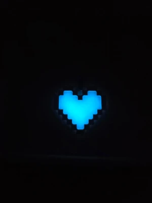 Pixelhjärta Glow in the dark hjärthalsband - Unikt halsband med ett pixelhjärta som lyser i mörkret. Hängsmycket är vitt i dagsljus och får en cool blå glow när det är mörkt. Kedjan och ramen är i silverfärgad metall och har en modern, kantig design. Perfekt accessoar för dig som gillar gaming eller retrostil. Kedjan är I rostfritt stål. Hänget börjar lysa i mörker efter att ha varit en kort stund i vanligt dagsljus. Lyser vanligtvis i flera timmar. 