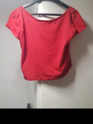 Röd croppad topp med vid urringning - Snygg röd croppad topp med korta ärmar och bred, öppen i ryggen Perfekt att styla med höga jeans eller kjol. Tillverkad i mjuk bomull för en bekväm känsla. Storlek: S