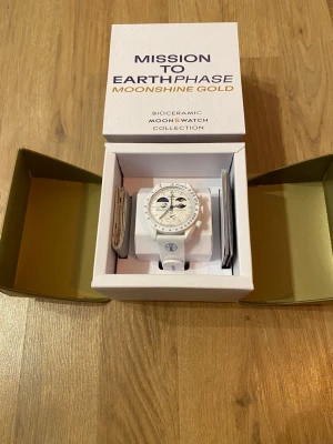 Omega x Swatch MoonSwatch Moonshine Gold Snowflake - Säljer en vit Omega x Swatch MoonSwatch Mission to Earthphase Moonshine Gold. Klockan har biokeramisk boett, vit textilrem och detaljer i guld på urtavlan. Snygg och unik design med månfaskomplication och tydliga index. Kommer i originalbox.