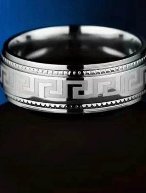 Silverfärgad ring med grekiskt mönster - Stilren ring i silverfärgad metall med ett klassiskt grekiskt nyckelmönster runt hela ringen. Ringen har blanka kanter och en mattare mittdel med det ingraverade mönstret. Perfekt för dig som gillar tidlös och unik design. stainless steel