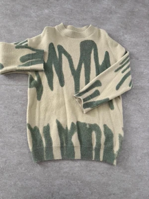 Stickad grön tröja, storlek M - Säljer denna coola stickade tröjan med ett abstrakt grafiskt mönster. Modellen är skönt oversized med en avslappnad och modern look.  Storlek M. Fint skick, finns ett jättelitet hål (se bild)💚