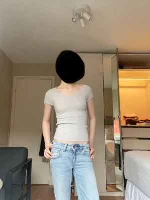 Ljusgrå ribbad kortärmad topp - Snygg ljusgrå ribbad topp med korta ärmar och rund och lite nerdragen halsringning. Figurnära passform och croppad längd, perfekt till jeans eller kjol. Enkel och stilren design som passar till många olika looks.