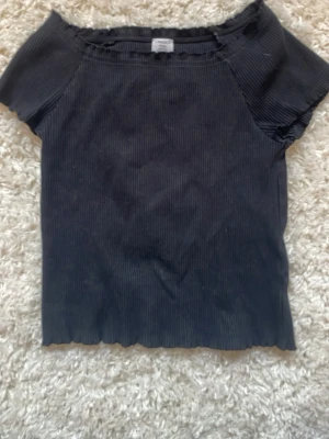 Svart ribbad topp  - En svart ribbad topp från Lindex med korta ärmar och rund hals. Toppen har en croppad passform och lätt vågig kant nedtill. Perfekt till jeans eller kjol för en enkel och stilren look.