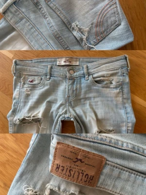 Ljusblå slitna jeans från Hollister - Säljer ett par ljusblå jeans från Hollister med snygga slitningar och hål på benen. Jeansen har klassisk femficksmodell, låg midja och skinny fit. Tillverkade i mjuk denim med stretch för extra komfort. Perfekta för en avslappnad och trendig look.