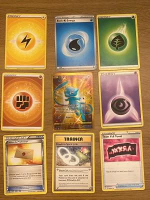 Pokémonkort samling med energi och tränare - Samling med nio Pokémonkort, inklusive olika energikort i färgerna gul, blå, grön, orange och lila, samt tränarkort och ett holografiskt Mew-kort. Korten har klassisk Pokémon-design med färgstarka illustrationer och text på både engelska och franska.