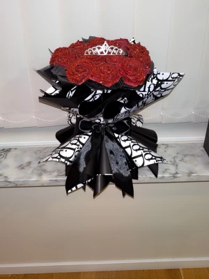 Bukett med röda glittriga rosor och tiara - Elegant bukett med  röda glitter rosor  dekorerad med en silverfärgad tiara. Buketten är inslagen i svart och vitt papper med D logga och har ett stort svart sidenband. Perfekt som present eller dekoration.