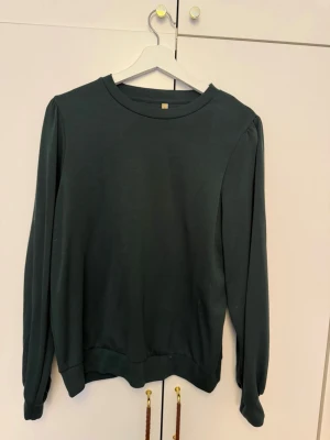 Mörkgrön sweatshirt från Soyaconcept - En stilren mörkgrön sweatshirt från Soyaconcept med rund halsringning och långa ärmar. Tröjan har en enkel, avslappnad passform och ribbade muddar vid ärmslut och nederkant. Perfekt för en casual look.