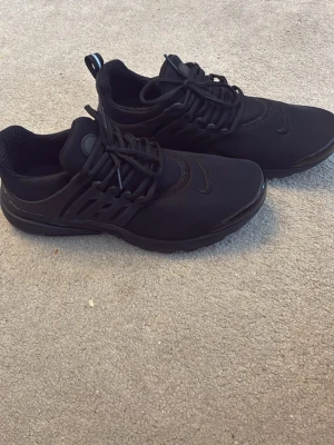 Svarta Nike Prestos sneakers.  - Snygga helsvarta Nike Prestos sneakers med låg profil och klassisk swoosh på sidan. Ovandelen är i mesh och syntetmaterial för skön känsla och bra andningsförmåga. Skorna har snörning och en sportig look som passar till det mesta.