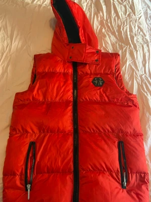 Röd dunväst från Philipp Plein - Snygg röd dunväst från Philipp Plein med huva och svarta detaljer i herr storlek. Perfekt för lager på lager och är i princip aldrig använd. ÄKTA, kvitto finns och medföljer med köp