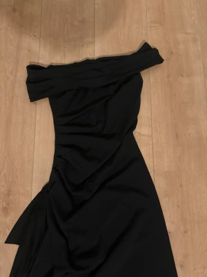 Svart offshoulder långklänning - Säljer en elegant svart långklänning med offshoulder-design och draperade detaljer. Klänningen har en figurnära passform och är perfekt för dig som vill ha en stilren och sofistikerad look. Materialet känns mjukt och följsamt.