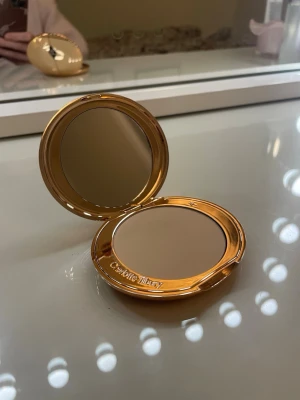 Charlotte Tilbury kompaktpuder - Säljer en puderfoundation från Charlotte Tilbury i en snygg guldig kompakt med spegel. Färgen är ljusbeige och formulan är pressat puder. Perfekt att ha i väskan för touch-ups under dagen. Lyxig och stilren design. Nypris 600kr