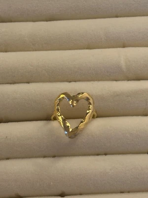 Guldfärgad ring med hjärtform - Trendig ring i guldfärgad metall med en öppen hjärtformad design. Ringen har en lite ojämn, organisk yta som ger en unik och modern känsla. Perfekt accessoar för dig som gillar statement-smycken och vill sticka ut.