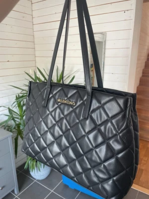 Svart Mario Valentino handväska - Säljer denna fina väska från Mario Valentino då jag inte använder den. Köpt av mig på zalando med nypris 1645kr, och mycket mycket sparsamt använd så inga synliga defekter. Finns många fack inuti och den rymmer t.ex skoldator och böcker! 🩷