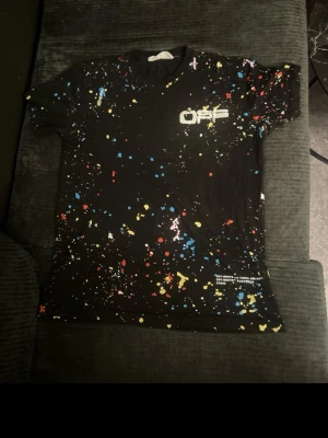 Off-White T-shirt – unik design - Off-White T-shirt – L – mycket bra skick  Säljer en Off-White t-shirt i storlek L. Använd endast 2–3 gånger, så den är i mycket fint skick utan fläckar, hål eller andra skador.  Modellen har ett snyggt svart basplagg med färgstänk-design och Off-White-logga framtill – en stilren och populär design som sticker ut.  • Storlek: L   • Skick: Mycket bra (nästan som ny)   • Färg: Svart med färgdetaljer     Pris: 300 kr (kan diskuteras vid snabb affär)