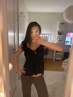 Svart topp med knyt från 157 - Supersnygg svart topp från 157 med volangärmar och knyt framtill. Toppen har en lätt rynkad struktur och är lite lösare i passformen. Perfekt att styla med jeans eller kjol för en trendig look.