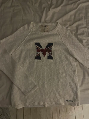 Vit tröja med M-tryck från Morris - Vit långärmad tröja från Morris med ett stort M på bröstet i Union Jack-mönster. Materialet är stickat och ger en avslappnad men snygg look.