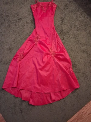 2000s dress/ bal klänning - Snygg röd långklänning med tunna axelband och v-ringad urringning. Klänningen har fina broderade blommor upptill och på kjolen, samt en lätt glansig finish. Perfekt för dig som vill sticka ut med en elegant och feminin look. Ny och oanvänt. 2000s klänning